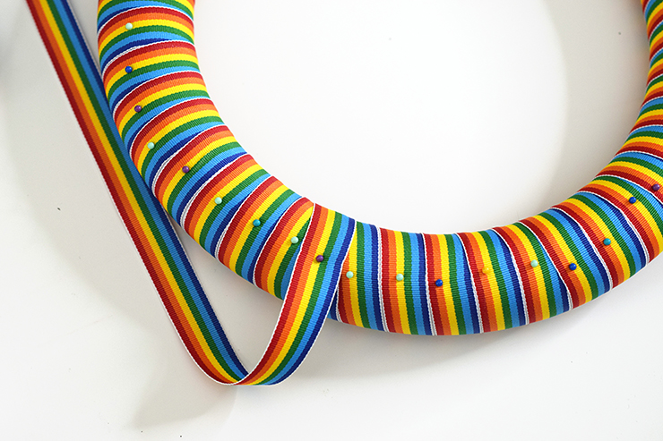 Rainbow ribbon looped around wreath form, held in place with straight pins.